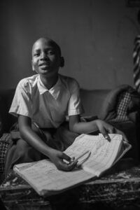 Amina, a former Play Lab participant, looks up from writing in a homework book from her elementary school