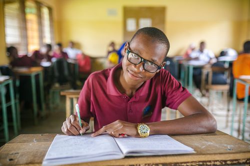 Boy smiling as he's writing on his desk in a school