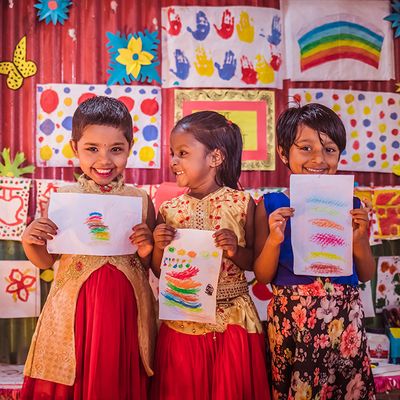 Three children in a Play Lab in Bangladesh hold up their colorful paintings and smile