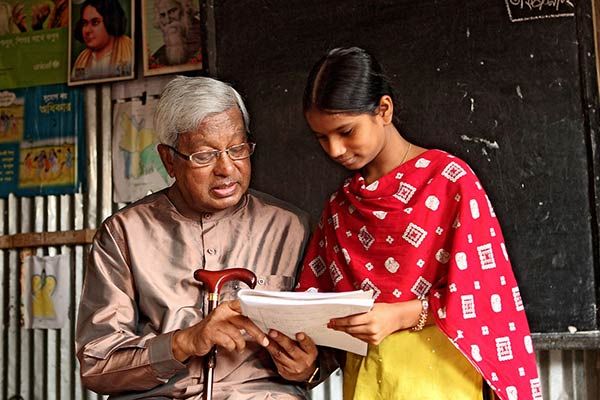 A man and a woman seated at desks in a classroom, engaged in discussion with educational materials around them.