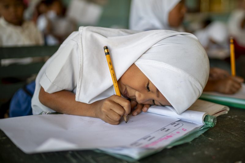 A young student in The Philippines writes on her paper