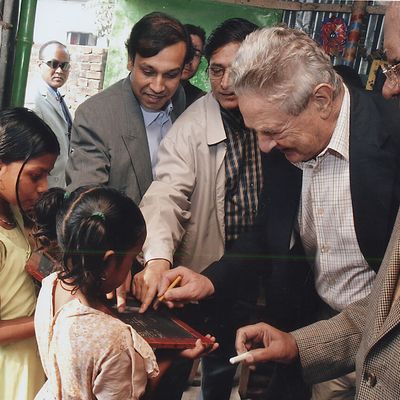 Philanthropist George Soros writing on a slate while sharing a playful moment with the students of BRAC school, accompanied by BRAC founder Sir Fazle Hasan Abed.