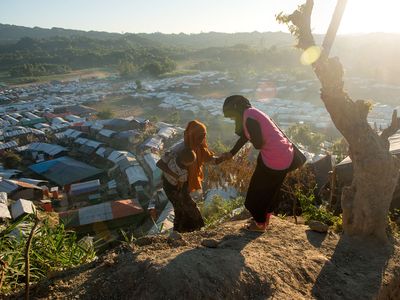 A BRAC staff gives a mother and her baby a helping hand in the Rohingya refugee camps in Cox's Bazar, Bangladesh during golden hour