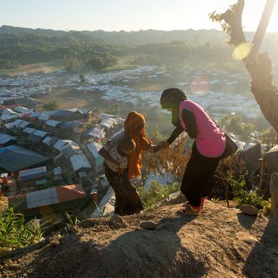 A BRAC staff gives a mother and her baby a helping hand in the Rohingya refugee camps in Cox's Bazar, Bangladesh during golden hour
