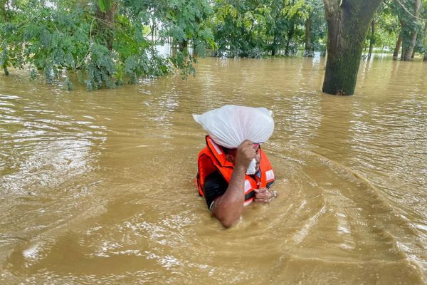 A BRAC frontline staff member wears an orange life jacket as he wades through chest-deep water to deliver aid supplies to families affected by the floods.
