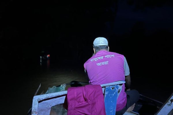 A BRAC staff member travels by boat after dark wearing a pink BRAC vest to reach families affected by flooding.