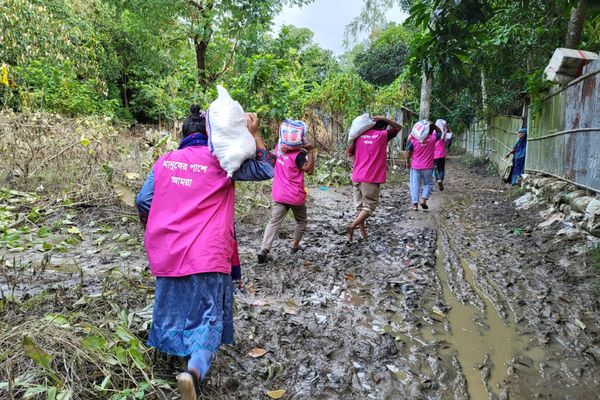 A BRAC team wearing BRAC's pink vests trudges through the mud in flood-stricken Chittagong, Bangladesh to deliver aid packages containing food and supplies to victims of the emergency.