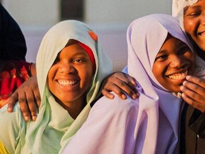 A group of four girls stand together laughing and smiling