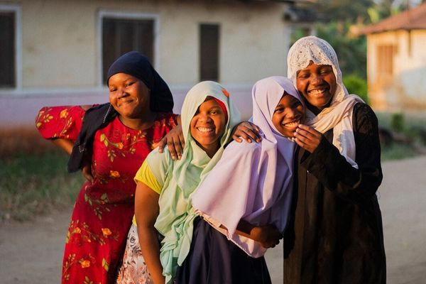 A group of four girls stand together laughing and smiling