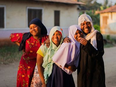 A group of four girls stand together laughing and smiling