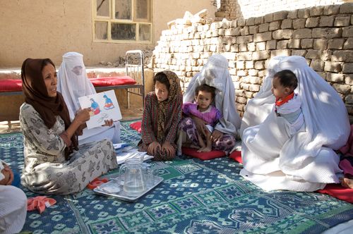 Health care workers showing images from a book to a seated audience with children