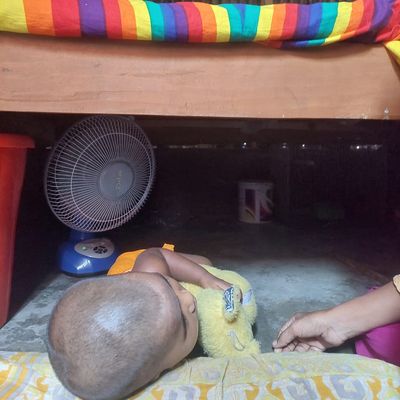 A toddler is kept under his bed – the coolest spot in his home – to escape the heat during the 2024 record breaking heatwave in May at Korail, the largest slum in Bangladesh.