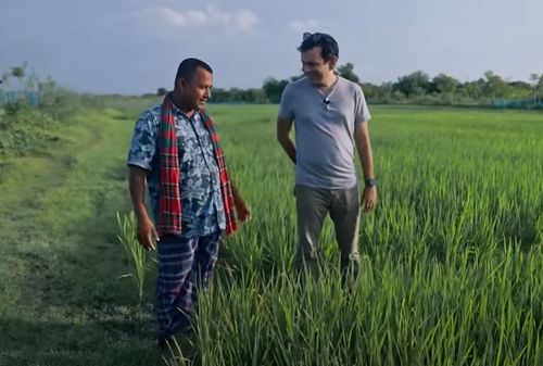 Asif Saleh stands with Mustakim bhai, a farmer, while learning about green paddy fields