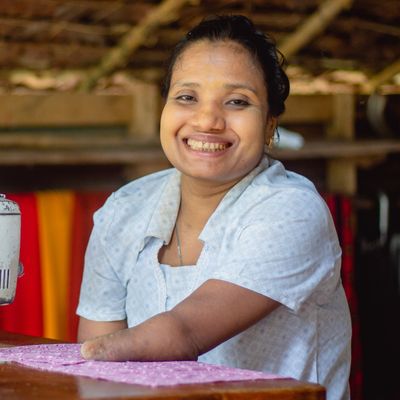 Zin, a participant in BRAC's microfinance program in Myanmar, smiles while she sits at her sewing machine.