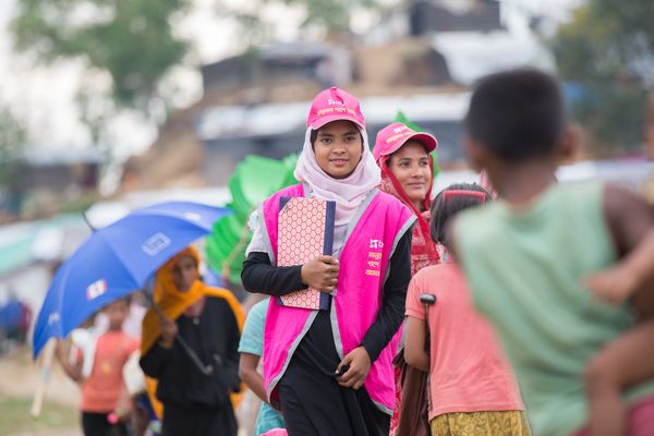 A BRAC staff member wearing a magenta vest and hat walk through the Rohingya refugee camps in Cox's Bazar, Bangladesh
