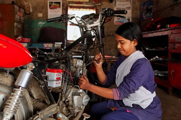 A woman in a purple outfit crouches in front of a motorcycle while she works to repair it