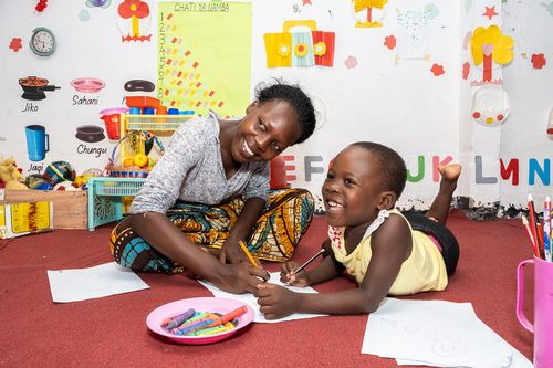 Woman and boy smiling on the floor in a school drawing together