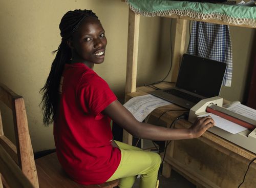 BRAC Rwanda microfinance client looking into camera as she operates a laptop and printer