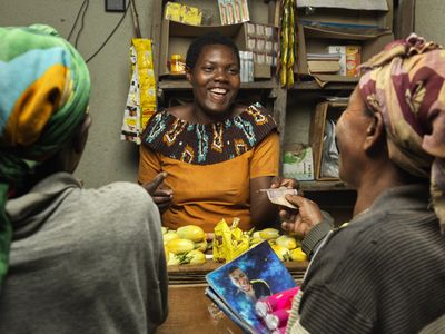 Three Rwandan women chat and laugh inside a grocery store during a transaction