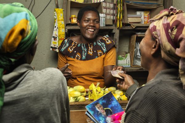 Three Rwandan women chat and laugh inside a grocery store during a transaction