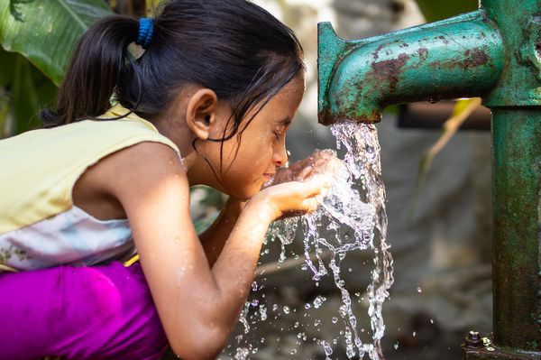 A child splashes safe water on her face from a tubewell