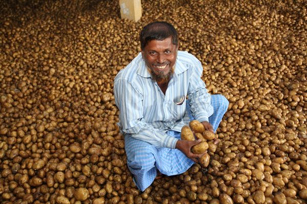 A man smiles as he sits amid potatoes being stored awaiting market