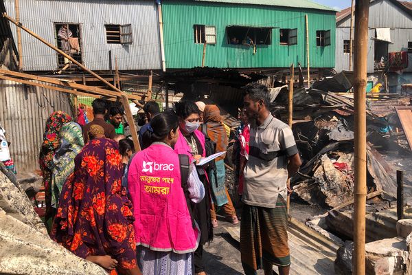 BRAC staff members meet with people impacted by the Korail fires. In the background the remains of burned structures.