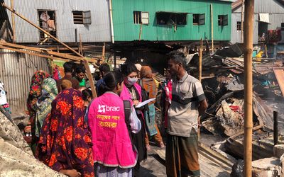 BRAC staff members meet with people impacted by the Korail fires. In the background the remains of burned structures.