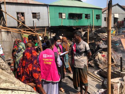 BRAC staff members meet with people impacted by the Korail fires. In the background the remains of burned structures.