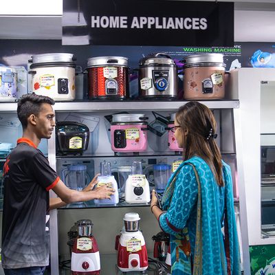 A young man works in an appliance store and speaks to a woman about a kitchen mixer