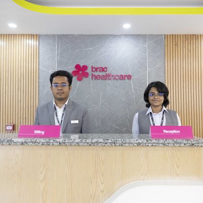 Two BRAC Healthcare staff members stand ready to welcome patients at the reception desk