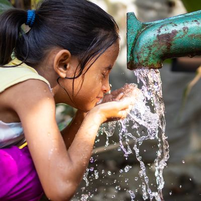 A young girl splashes her face as water pours from a faucet