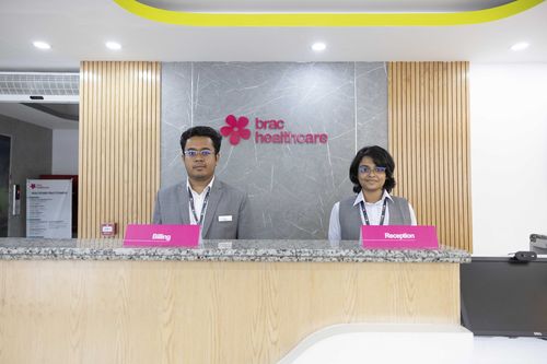 Two BRAC Healthcare staff members stand ready to welcome patients at the reception desk