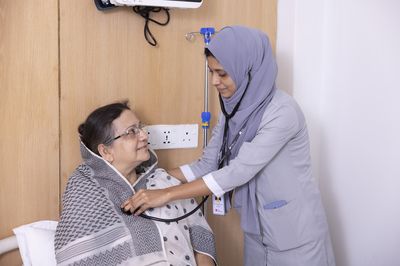 A female doctor listens to a patient's chest. The patient smiles at the doctor.