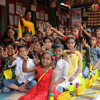 Children in a colorful classroom sit together and give peace signs to the camera