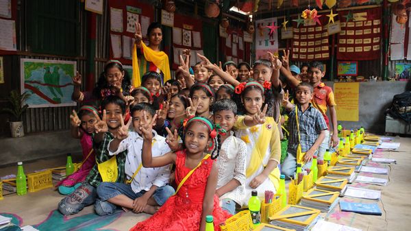 Children in a colorful classroom sit together and give peace signs to the camera