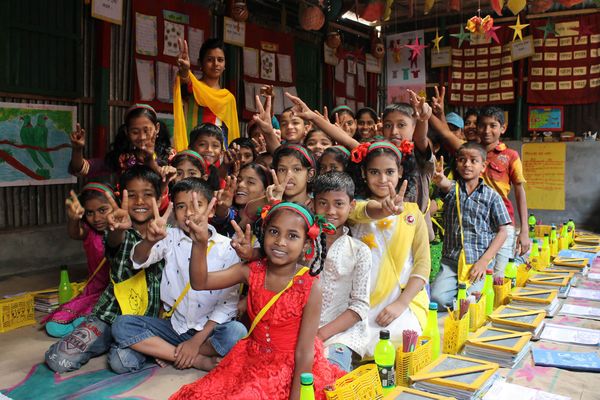 Children in a colorful classroom sit together and give peace signs to the camera