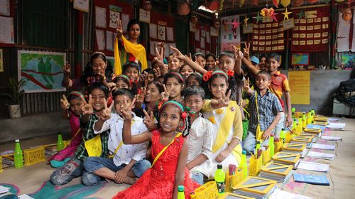 Children in a colorful classroom sit together and give peace signs to the camera