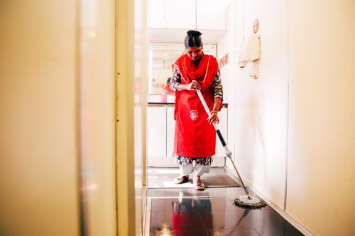 A woman wearing red carefully washes the floor of a Bhumijo toilet facility