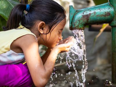 A young girl splashes her face as water pours from a faucet