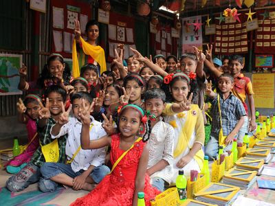 Children in a colorful classroom sit together and give peace signs to the camera