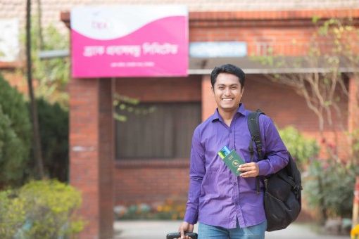 A man smiles as he stands outside of a Probashbandhu center, holding his green, Bangladshi passport