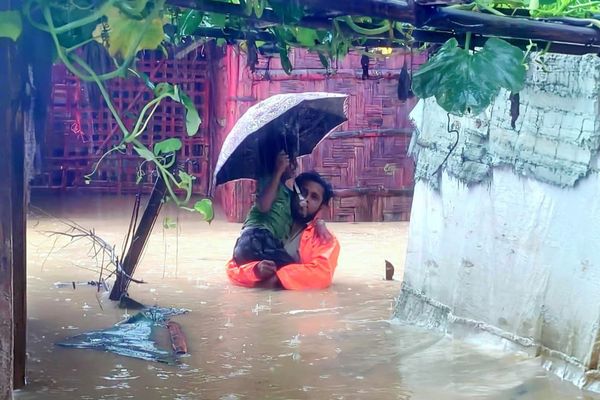 A man carries a small child down a flooded pathway in the Rohingya Refugee camps