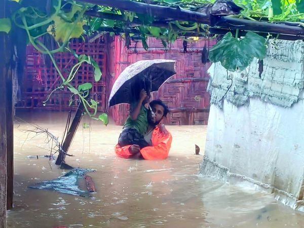 A man carries a small child down a flooded pathway in the Rohingya Refugee camps