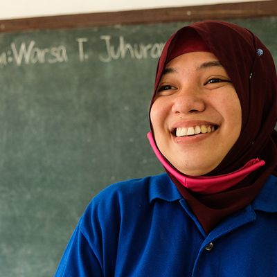 A BRAC teacher in the Philippines smiles in front of a chalk board