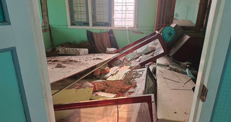 In a wall with teal green walls, a mix of furniture is toppled over and strewn across the floor. One bureau in the back corner is upright and has a mirror, in tact.