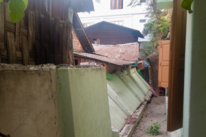 An image of a narrow alleyway between buildings with a toppled green concrete wall that has collapsed.