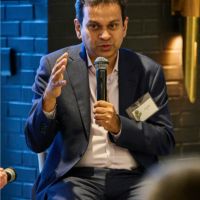 Asif Saleh, Executive Director of BRAC, speaks into a microphone while sitting on a stool at an UN week side event.