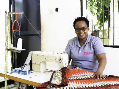 Woman Microfinance client with sewing machine smiling wearing a BRAC t-shirt