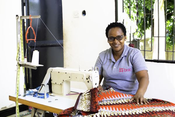 Woman Microfinance client with sewing machine smiling wearing a BRAC t-shirt